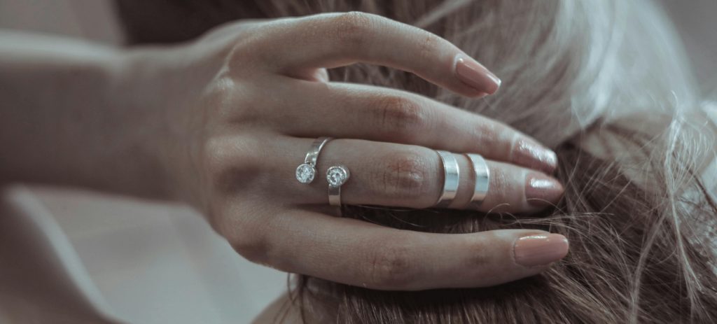 Unrecognizable crop female showing silver rings with precious stone while gently touching hair
