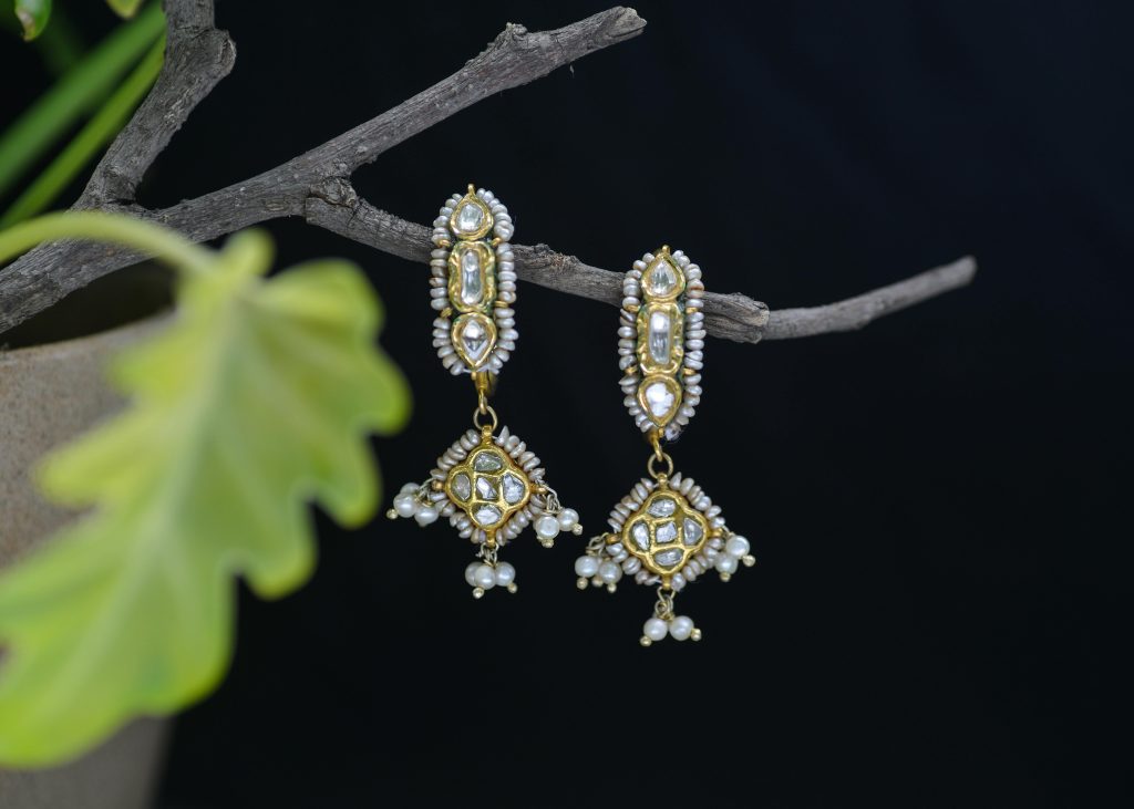 Luxurious pearl and gemstone earrings elegantly displayed on a natural branch with a dark backdrop.