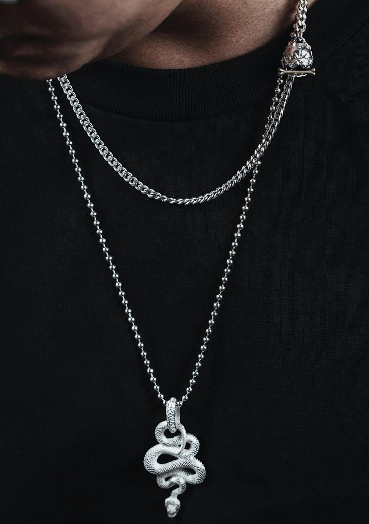 Elegant snake pendant on a silver chain necklace worn by a man, captured in a close-up shot