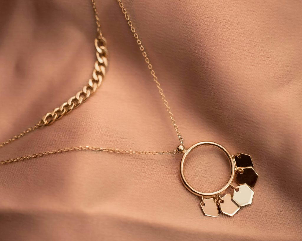 Close-up of a stylish gold necklace with hexagonal charms on textured fabric, showcasing elegance.