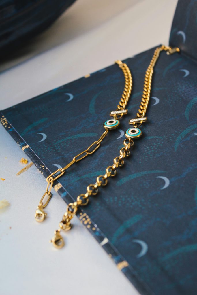 Two stylish gold necklaces displayed on a dark blue patterned surface, showcasing elegance and luxury.