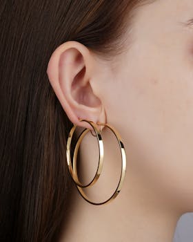 Elegant close-up of a woman's ear adorned with large gold hoop earrings, showcasing jewelry fashion.