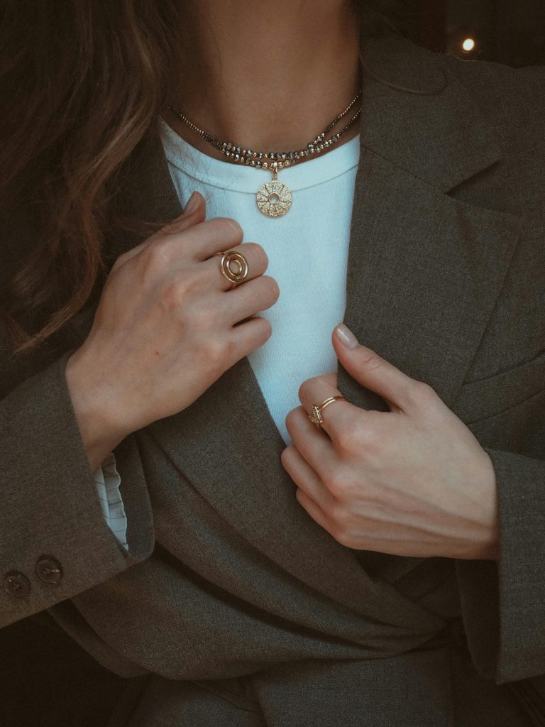 Elegant layered necklaces and rings on a woman wearing a chic blazer, highlighting fashionable accessories.