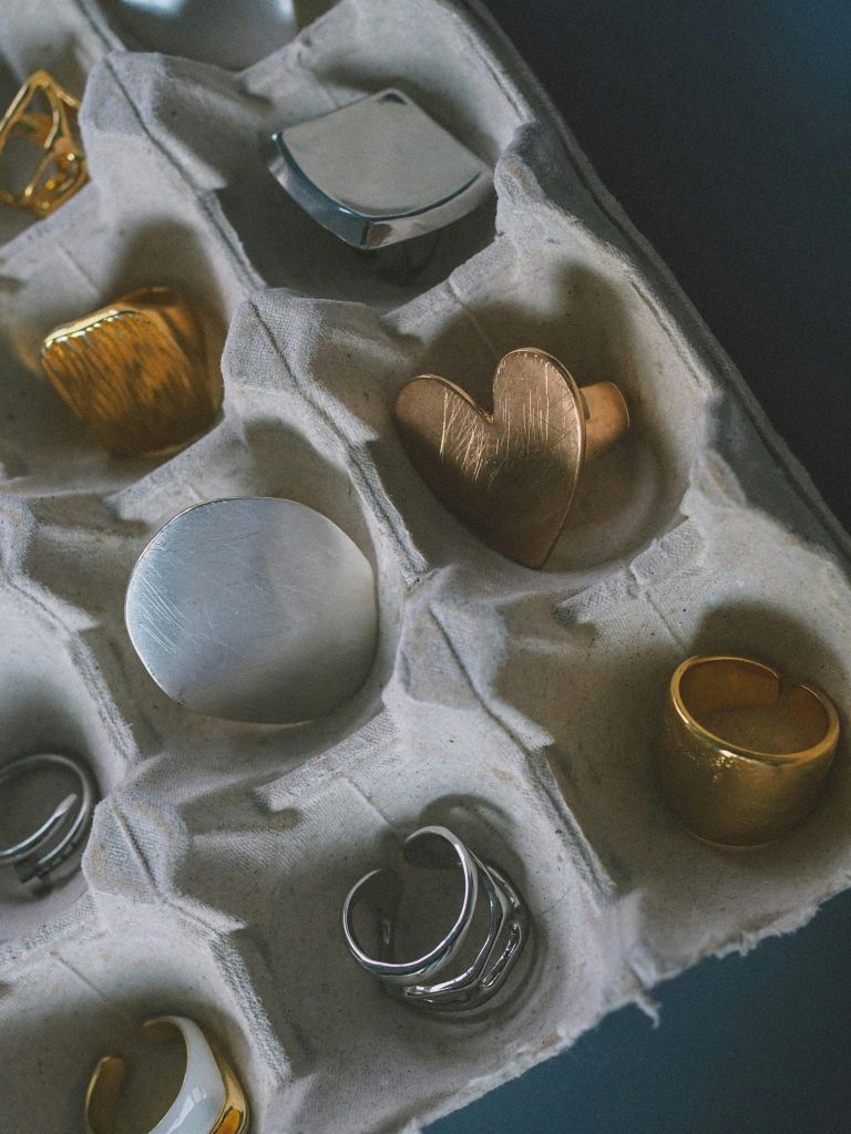 A variety of gold and silver rings creatively displayed in a paper egg carton.