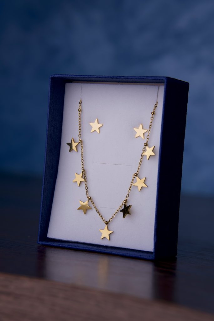 Gold star-shaped necklace and earrings in a blue box on a dark wooden surface.