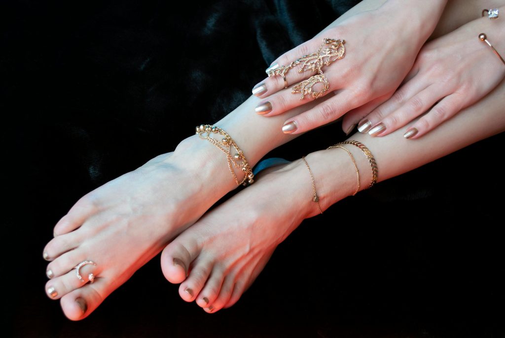 Crop anonymous female legs and hands with stylish manicure and pedicure wearing oriental golden bracelets anklets and rings