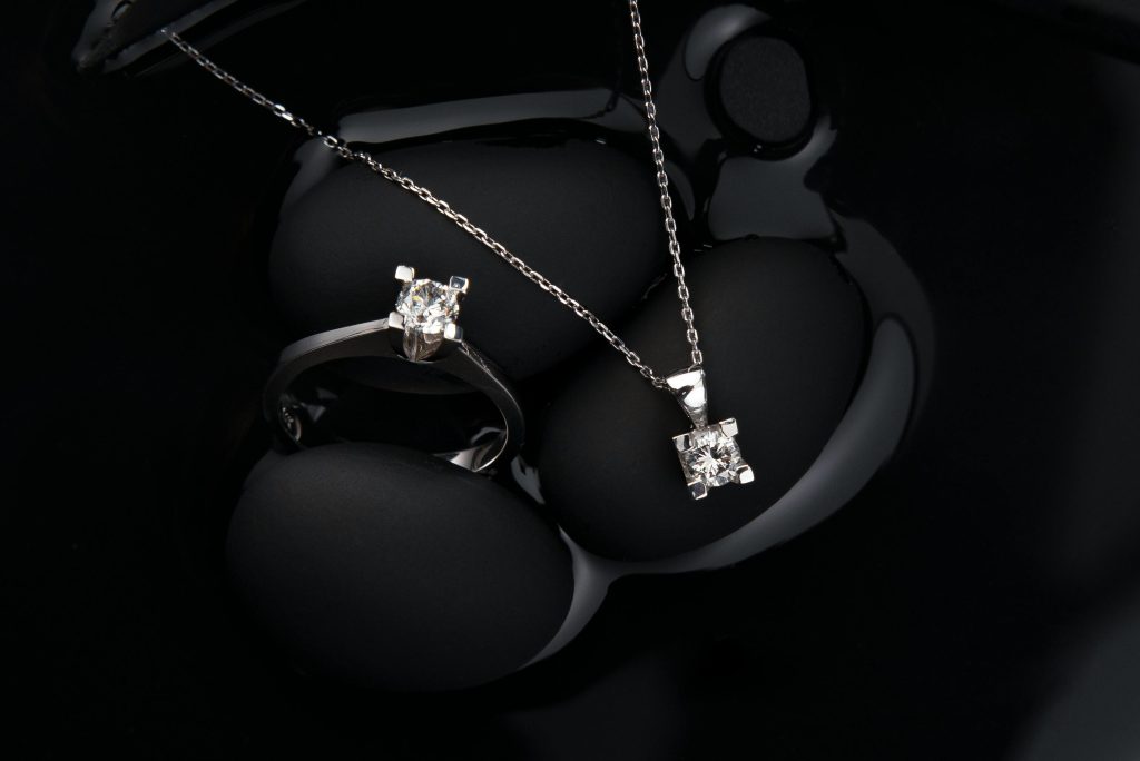Luxurious silver diamond ring and pendant necklace on a black background, showcasing elegance and sophistication.